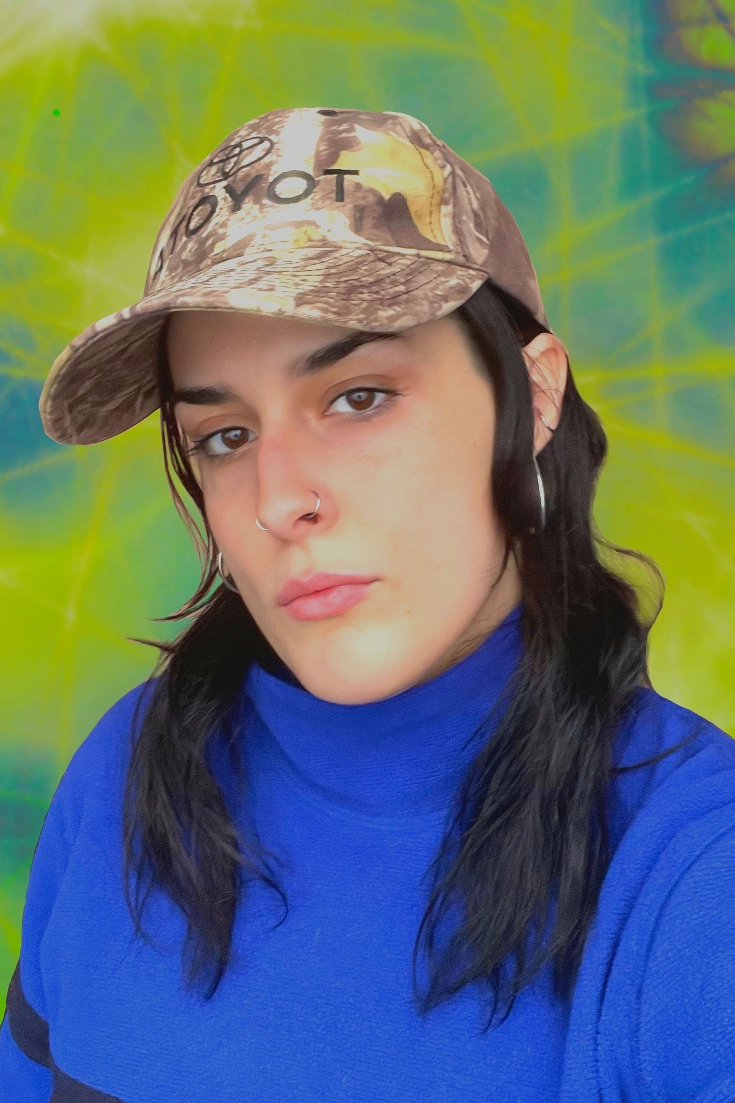 Person wearing a camouflage cap with a brand logo against a colorful, abstract background